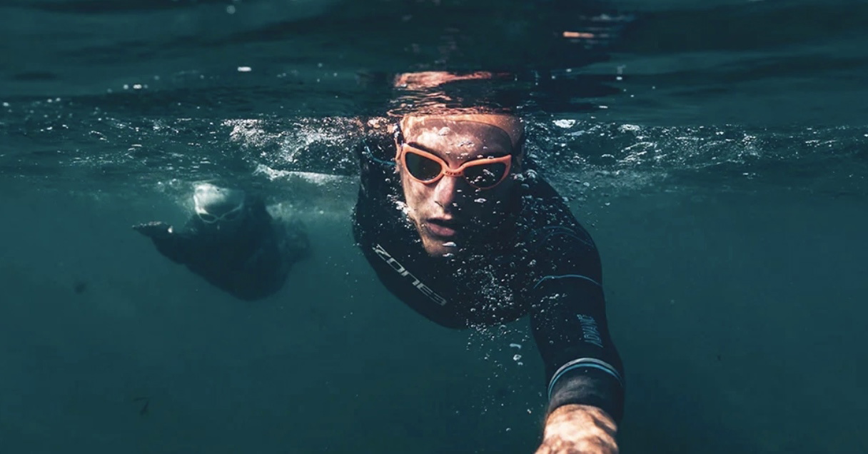 Onderwateropname van een zwemmer in een zwart wetsuit met zwembril die naar de camera toe zwemt