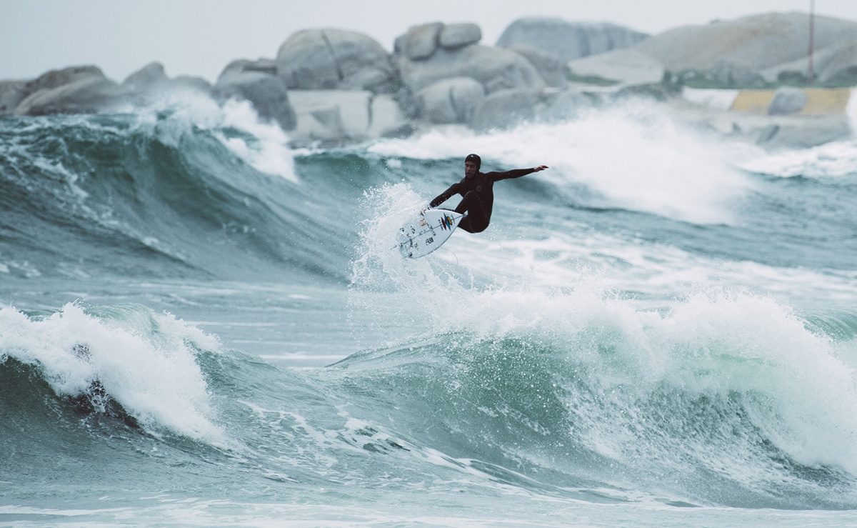 Surfer in een winterwetsuit met hood loopt het koude water in