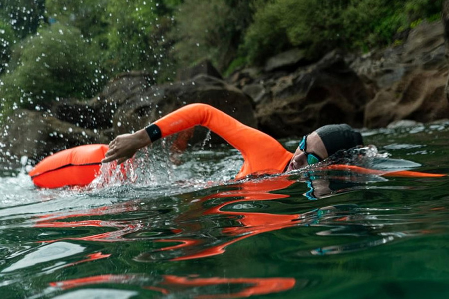 Openwaterzwemmer in een wetsuit met fluororanje mouwen die borstcrawl zwemt achter een oranje zwemboei