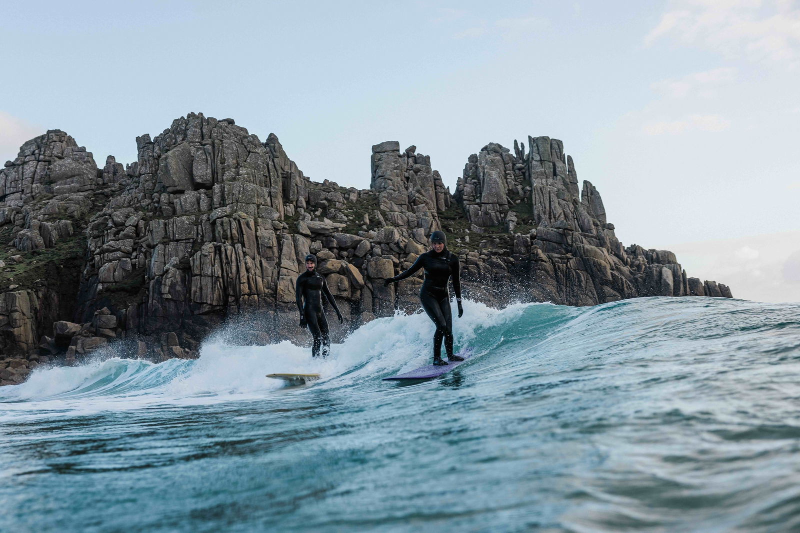 Surfer op een kleine gladde golf onder hoge granieten kliffen