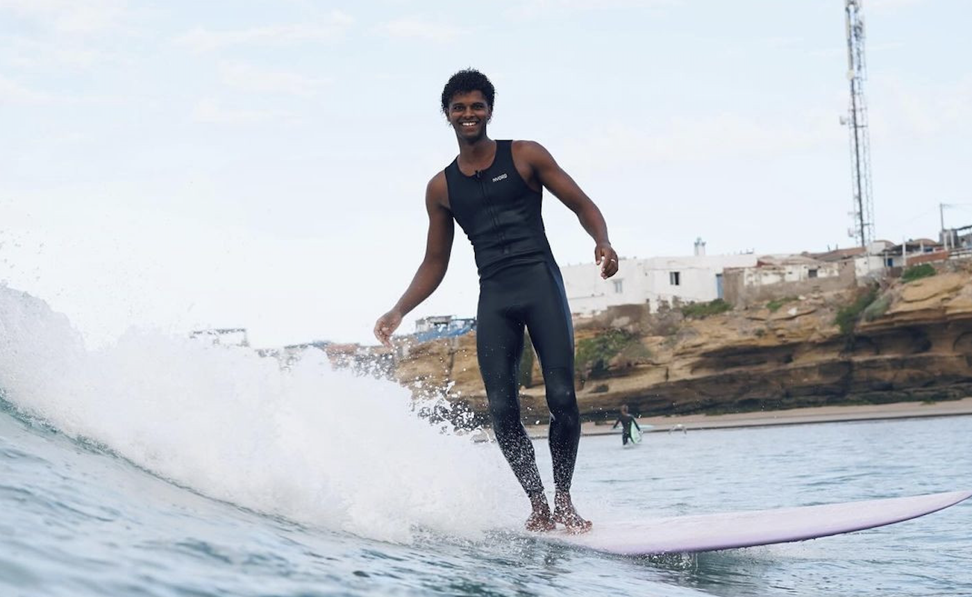 Surfer in een mouwloos zwart wetsuit rijdt op een longboard door het schuim