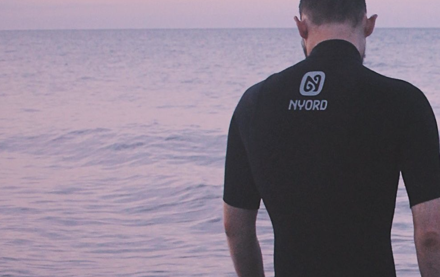 Close-up van de rug van een zwart Nyord wetsuit met korte mouwen tegen een roze ochtendlucht