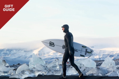 Surfer in winterwetsuit met hood draagt zijn surfboard door de duinen