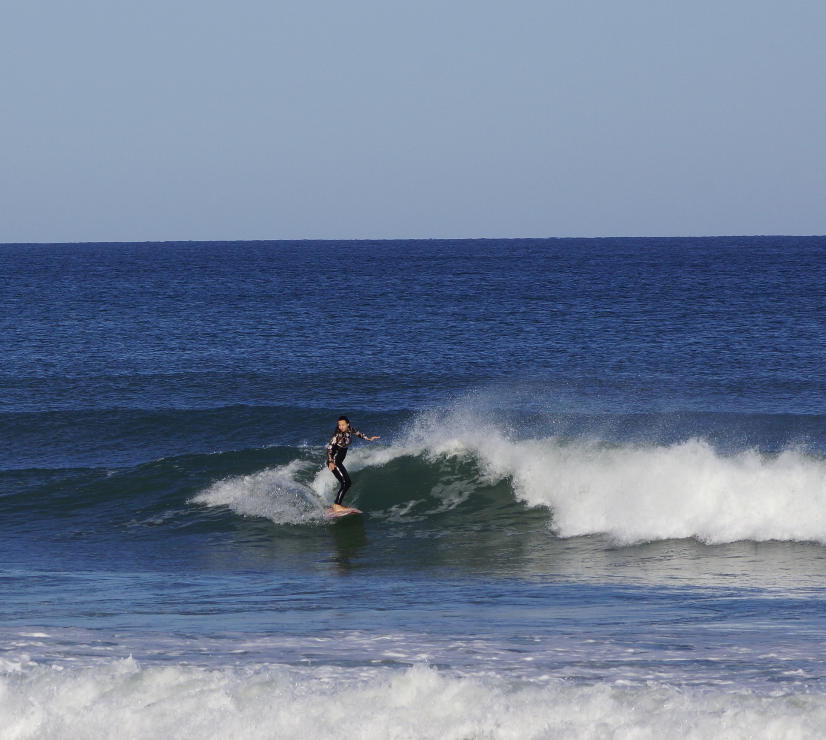 Lone surfer trimming along the face of a small blue wave on a sunny day