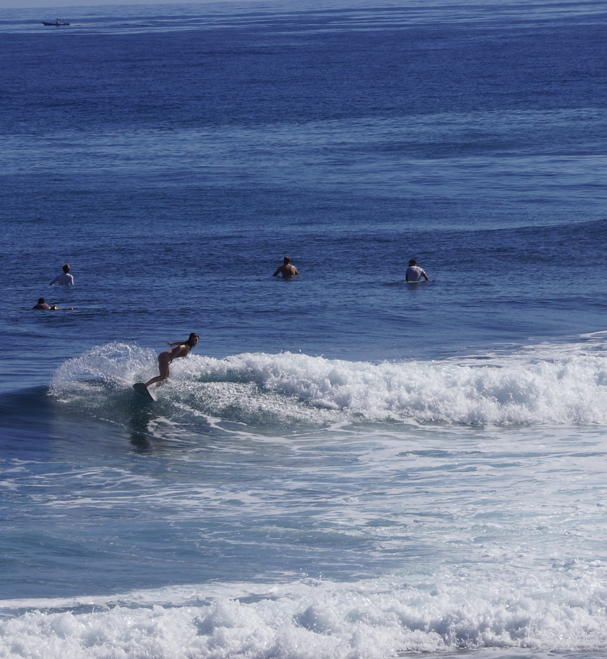 Surfer riding a small crumbling wave with others waiting out in the line-up behind