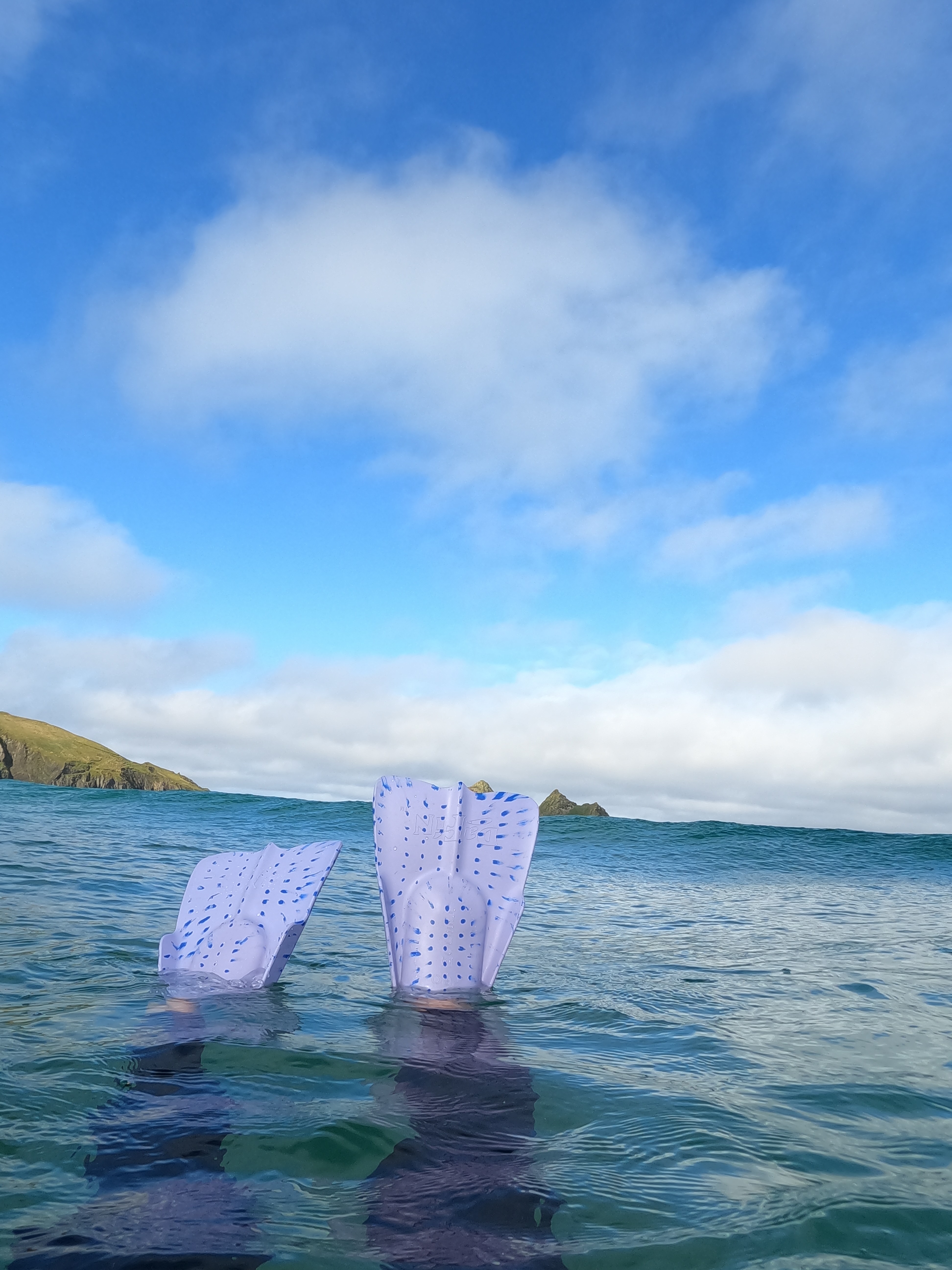Pair of pale purple swim fins breaking the surface as a swimmer duck-dives near the headland