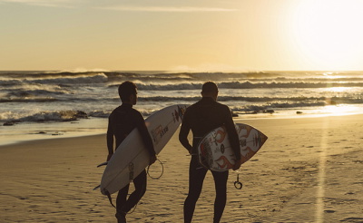 Surfers in wetsuit als silhouet tegen een zonsondergang