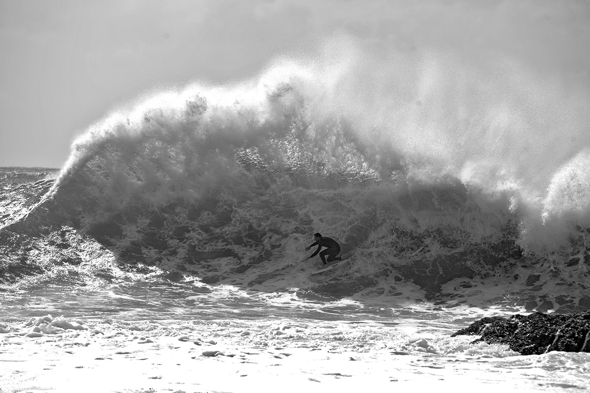 Black and white shot of a surfer racing along the base of a huge feathering wave