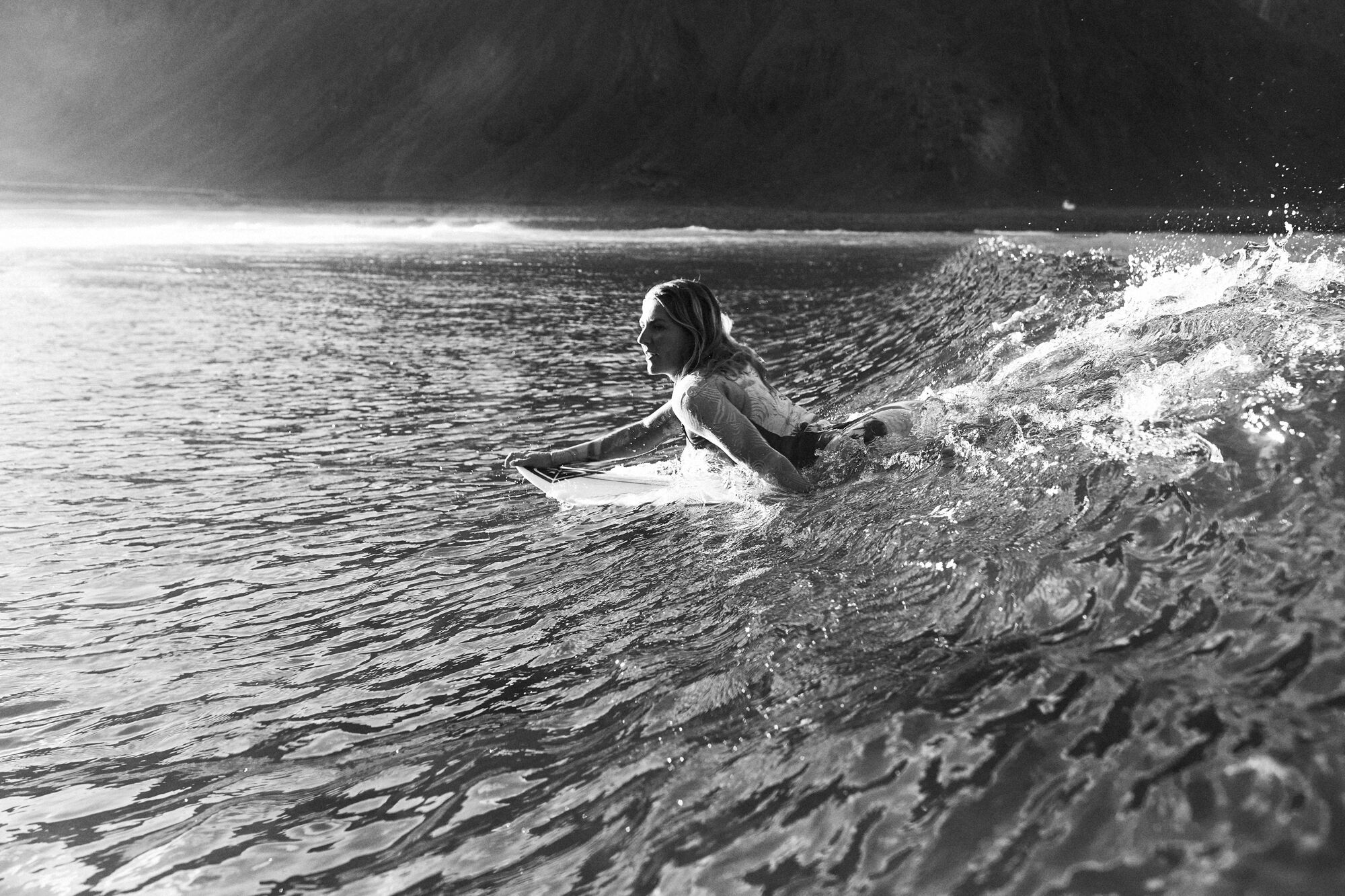 Black and white image of a surfer carving through spray on a backlit wave